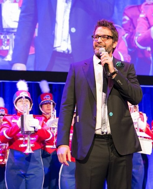 Peter Hermann, the evening's host, stands in front of the Spirit of Stony Brook Marching Band. Photography by: Michael Webber